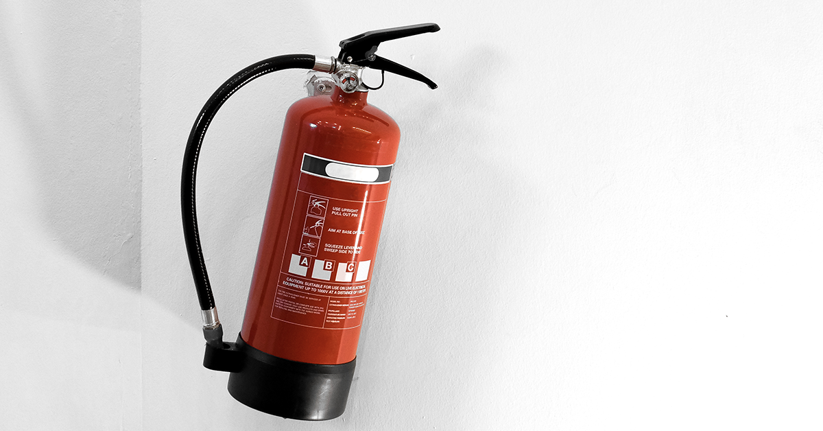 A technician attaches a service certificate to a red fire extinguisher on a workbench with tools.