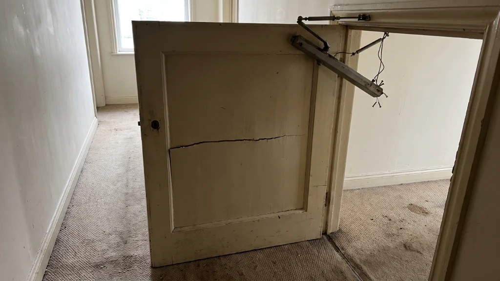 A cracked fire door with a broken self-closer in a shared HMO hallway, the kind of defect found in real enforcement cases