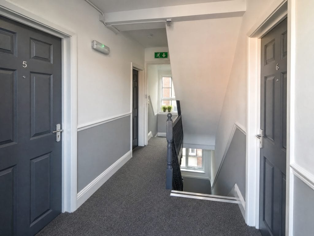 A clear communal stairwell and corridor in a UK residential block showing fire exit signage and an emergency light fitting